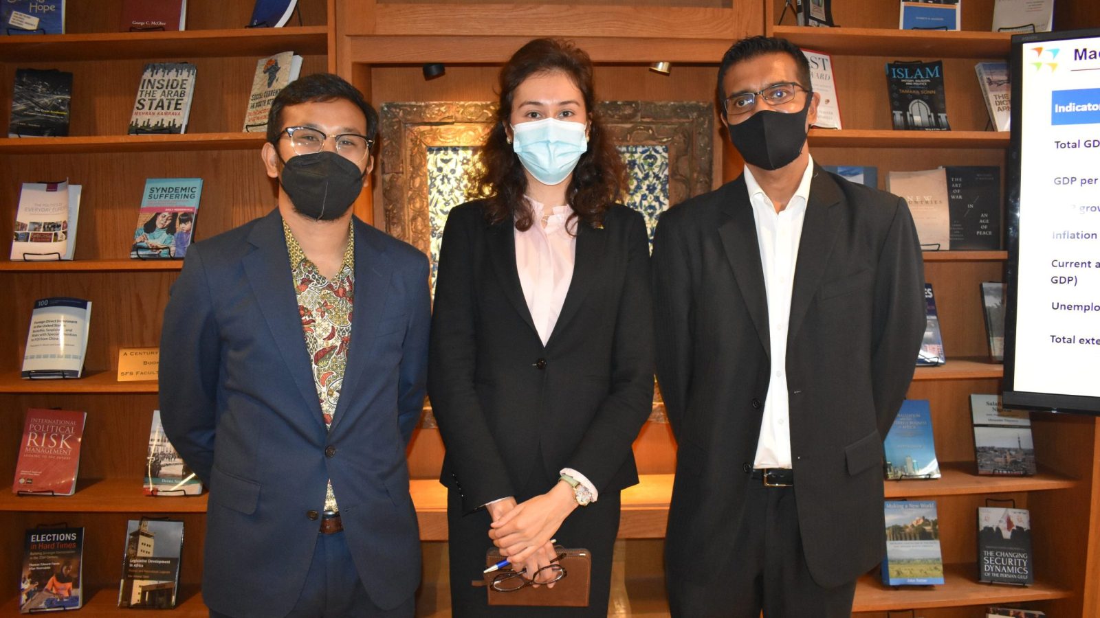 Putra and Kamilla standing with Partish Halady wearing business attire in front of bookshelf in a library.