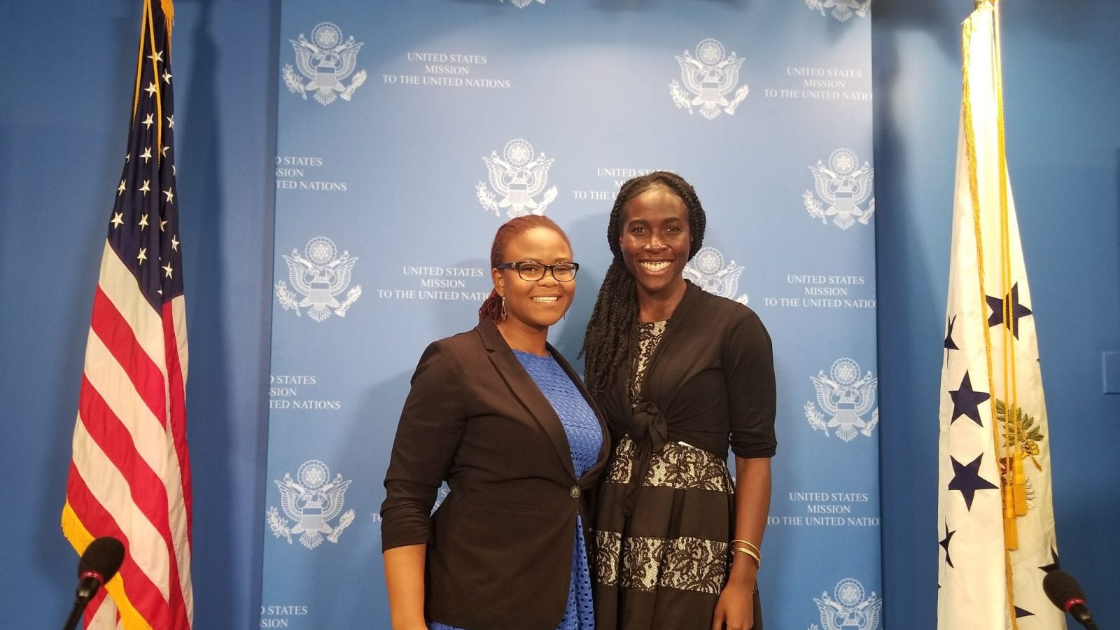 Yoluyinka and a colleague standing in front of a UN logo backdrop