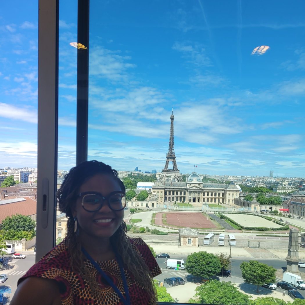 Foluyinka smiling in front of a backdrop of Paris with the Eiffel Tower