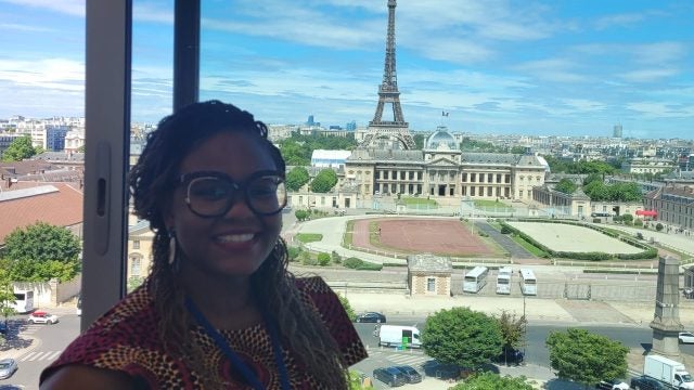 Foluyinka smiling in front of a backdrop of Paris with the Eiffel Tower