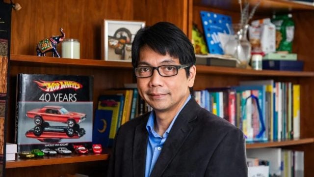 Professor Erwin Tiongson stands in front of a bookshelf displaying Hot Wheels cars